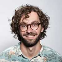 A man with curly hair and glasses is smiling.